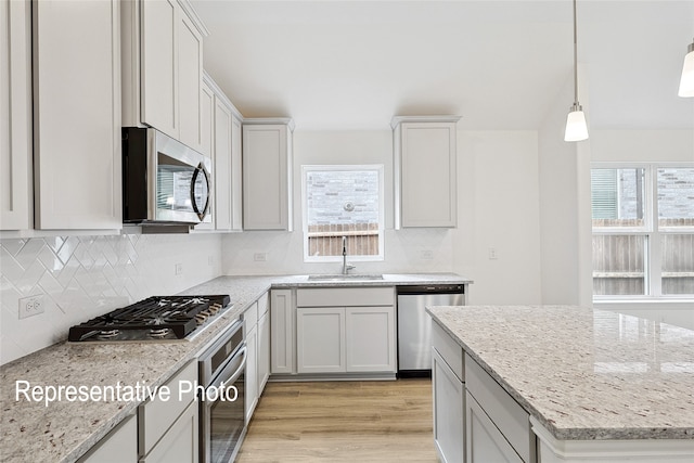 kitchen with sink, stainless steel appliances, light stone countertops, white cabinets, and decorative light fixtures