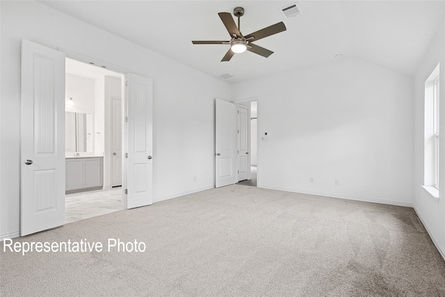 unfurnished bedroom featuring vaulted ceiling, light colored carpet, and ensuite bathroom