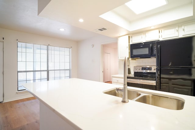 kitchen featuring sink, black appliances, light hardwood / wood-style floors, white cabinets, and decorative backsplash