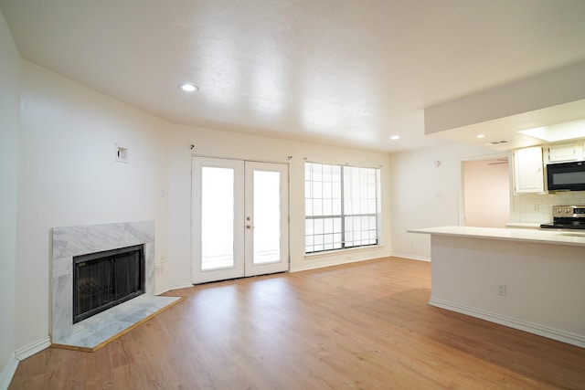 unfurnished living room with a high end fireplace, light hardwood / wood-style floors, and french doors