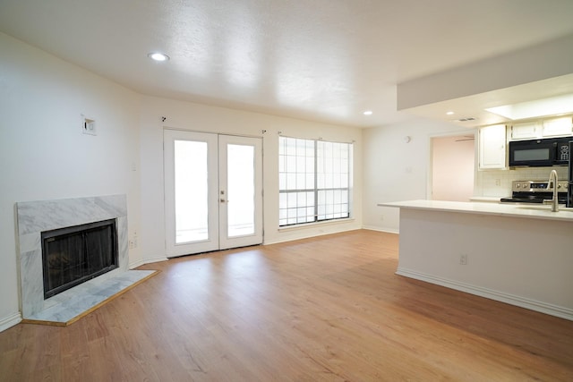 unfurnished living room featuring a premium fireplace, light hardwood / wood-style floors, and french doors