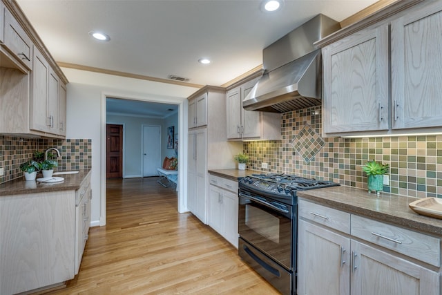 kitchen with light brown cabinetry, sink, black range with gas stovetop, wall chimney range hood, and light wood-type flooring