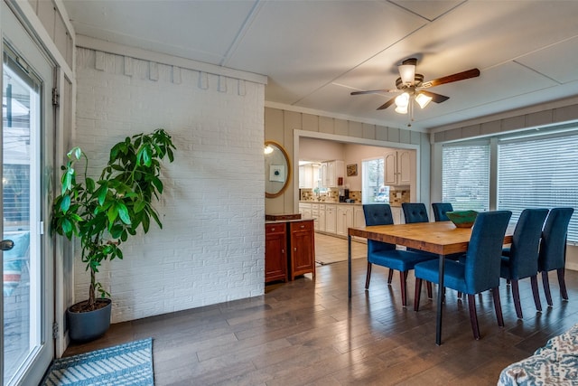 dining area featuring dark hardwood / wood-style floors, ceiling fan, and brick wall