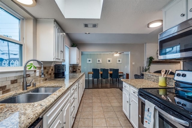 kitchen featuring appliances with stainless steel finishes, sink, white cabinets, light tile patterned floors, and light stone counters