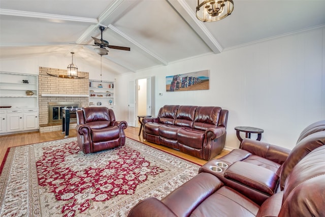 living room with vaulted ceiling with beams, light hardwood / wood-style flooring, ceiling fan, a brick fireplace, and built in shelves