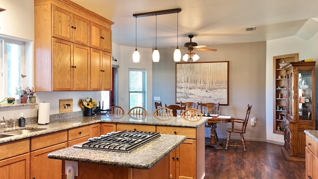 kitchen with pendant lighting, dark hardwood / wood-style floors, a center island, light stone countertops, and stainless steel gas cooktop