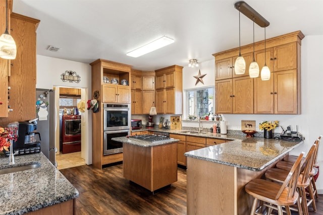 kitchen with pendant lighting, appliances with stainless steel finishes, a kitchen island, and dark stone counters