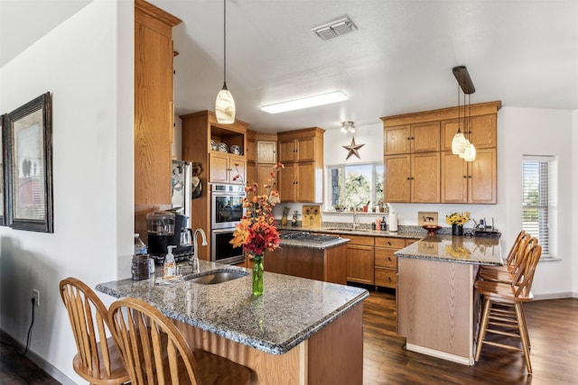 kitchen with a breakfast bar area, double oven, a center island, kitchen peninsula, and dark stone counters