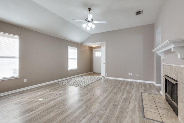 unfurnished living room featuring vaulted ceiling, a tile fireplace, light hardwood / wood-style floors, and ceiling fan