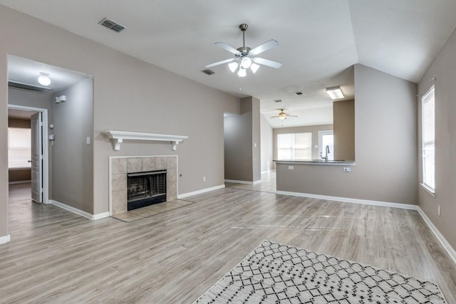 unfurnished living room with lofted ceiling, sink, ceiling fan, a tiled fireplace, and light wood-type flooring