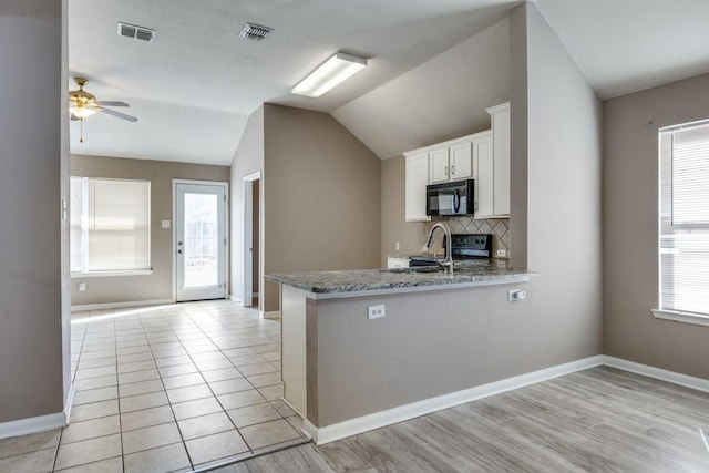 kitchen with lofted ceiling, tasteful backsplash, kitchen peninsula, light stone countertops, and white cabinets