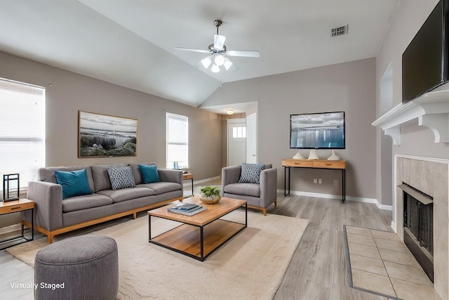 living room featuring vaulted ceiling, a tile fireplace, ceiling fan, and light wood-type flooring