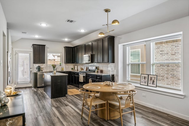 kitchen featuring hanging light fixtures, stainless steel appliances, a center island, light stone counters, and decorative backsplash