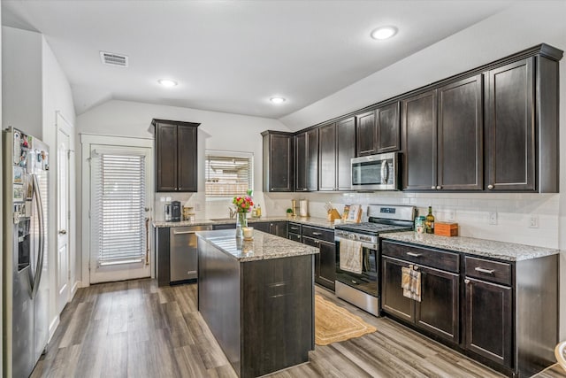 kitchen featuring lofted ceiling, light stone counters, a kitchen island, stainless steel appliances, and light hardwood / wood-style floors