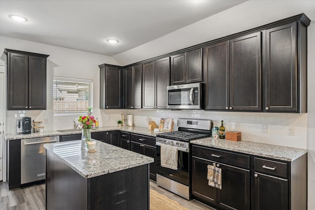 kitchen with light stone counters, vaulted ceiling, light wood-type flooring, a kitchen island, and stainless steel appliances