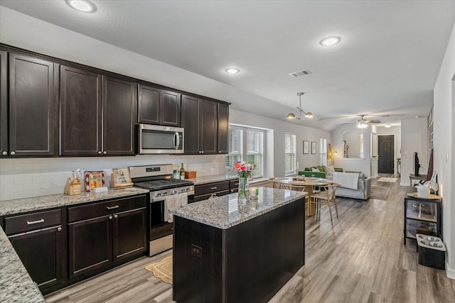 kitchen with a kitchen island, tasteful backsplash, stainless steel appliances, light stone countertops, and dark brown cabinets