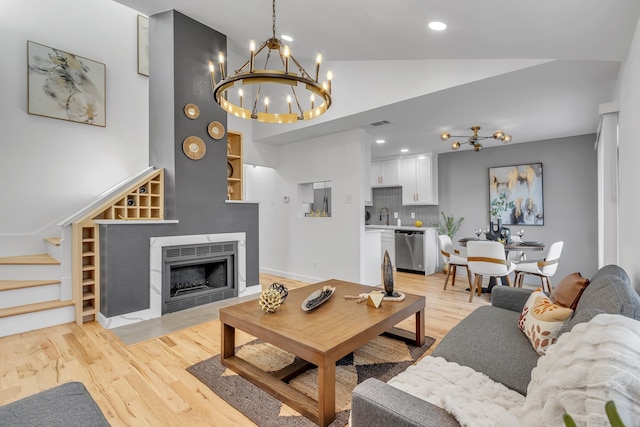 living room with a tile fireplace, vaulted ceiling, built in features, sink, and light hardwood / wood-style floors