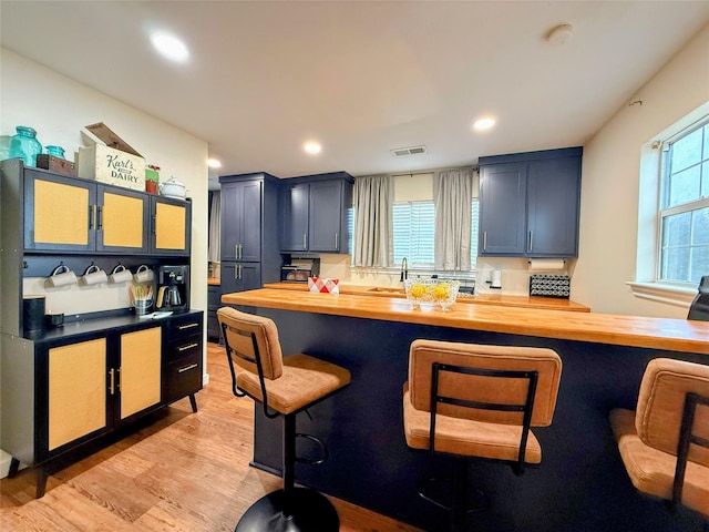 kitchen with blue cabinetry, wooden counters, a breakfast bar area, and light hardwood / wood-style flooring