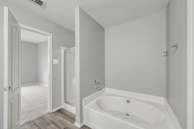 bathroom with hardwood / wood-style flooring, a textured ceiling, and separate shower and tub