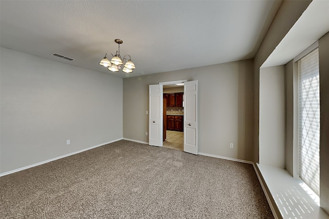 carpeted empty room featuring a textured ceiling and a chandelier