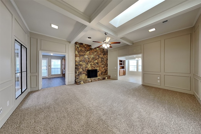 unfurnished living room featuring coffered ceiling, a stone fireplace, a skylight, light colored carpet, and beam ceiling