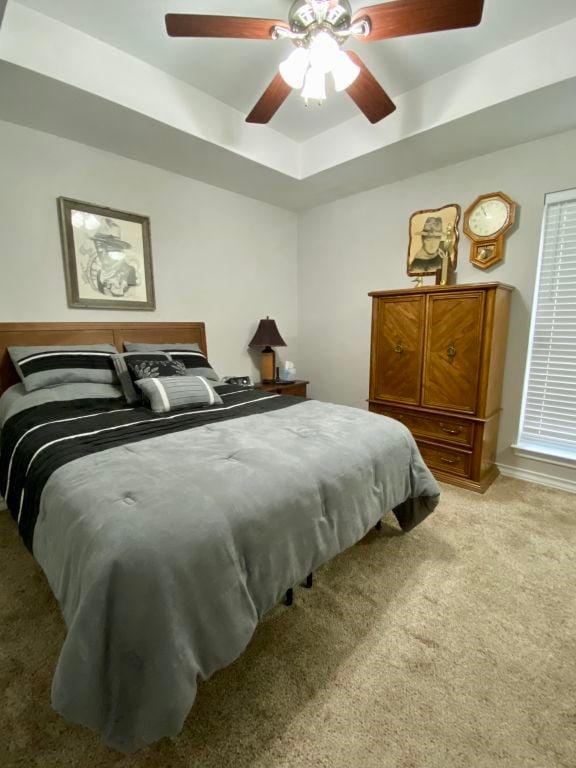 bedroom with ceiling fan, light colored carpet, and a tray ceiling