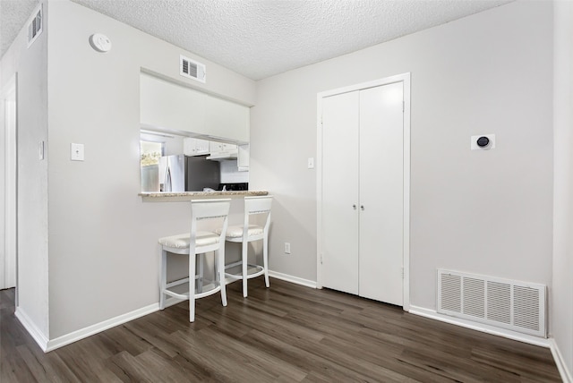 kitchen with a breakfast bar, dark hardwood / wood-style floors, white cabinets, stainless steel refrigerator with ice dispenser, and a textured ceiling