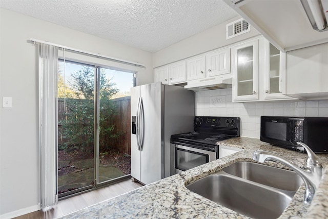 kitchen with sink, appliances with stainless steel finishes, white cabinetry, light stone counters, and decorative backsplash