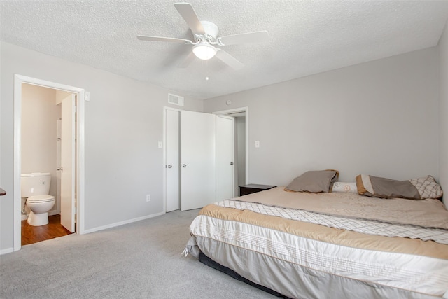 bedroom featuring ceiling fan, light carpet, a textured ceiling, and ensuite bath