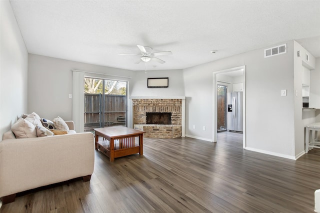 living room featuring ceiling fan, a textured ceiling, a fireplace, and dark hardwood / wood-style flooring