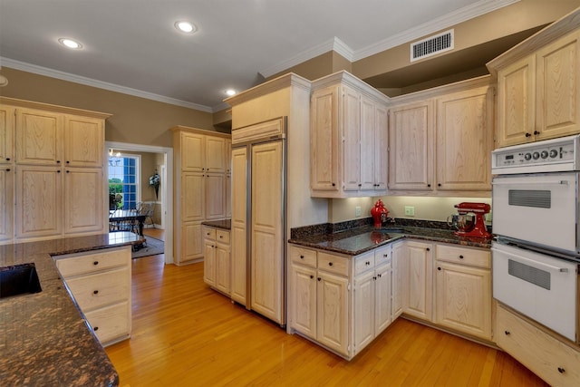 kitchen with light hardwood / wood-style flooring, light brown cabinetry, white double oven, and dark stone counters