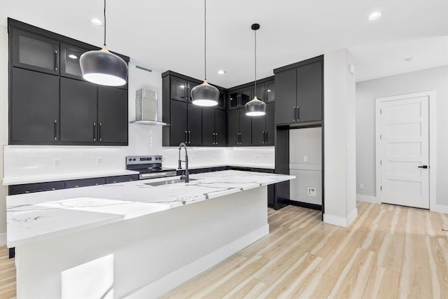 kitchen with sink, wall chimney range hood, a center island with sink, decorative light fixtures, and stainless steel range with electric cooktop