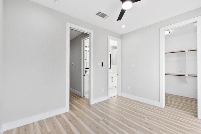 unfurnished bedroom featuring ceiling fan, a walk in closet, connected bathroom, and light hardwood / wood-style floors