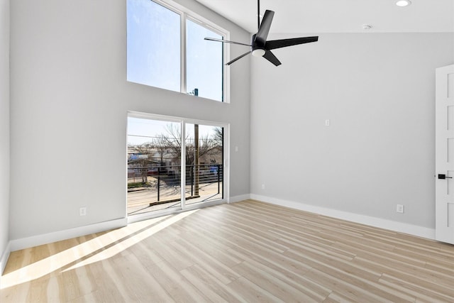 unfurnished living room featuring a towering ceiling, light hardwood / wood-style flooring, and ceiling fan