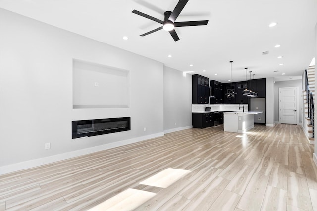 unfurnished living room featuring ceiling fan, sink, and light hardwood / wood-style flooring