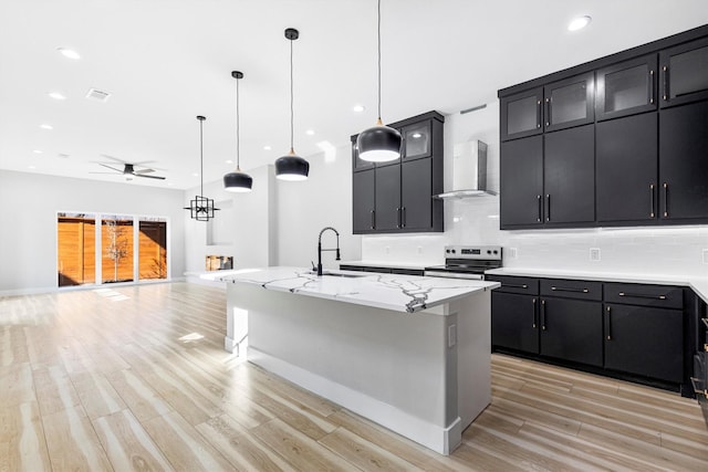 kitchen featuring a kitchen bar, a center island with sink, electric range, pendant lighting, and wall chimney range hood