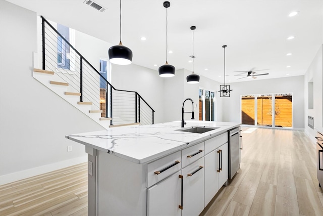 kitchen featuring an island with sink, dishwasher, sink, white cabinets, and hanging light fixtures