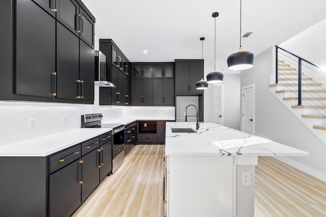 kitchen with pendant lighting, sink, backsplash, electric range, and an island with sink