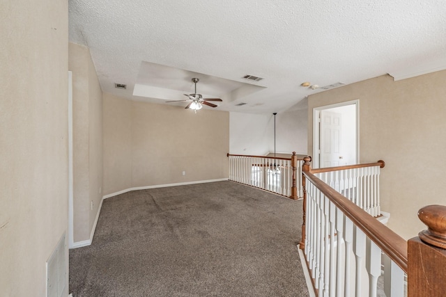 spare room featuring dark carpet, ceiling fan, a tray ceiling, and a textured ceiling