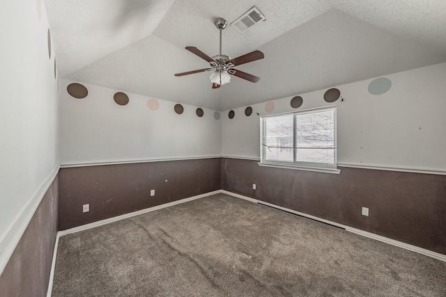 carpeted empty room featuring lofted ceiling, ceiling fan, wooden walls, and a textured ceiling