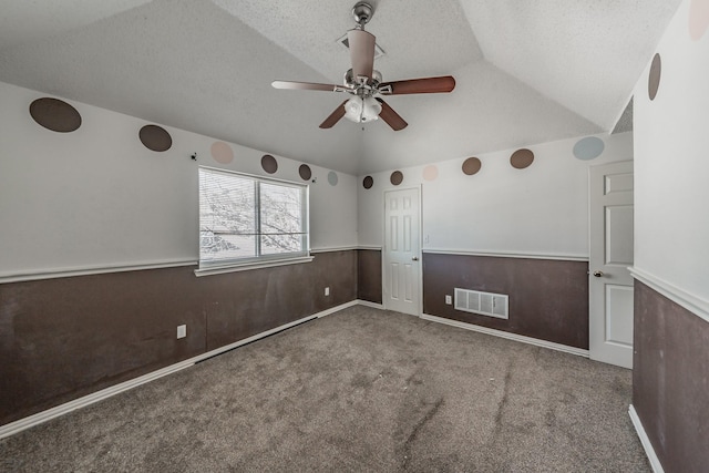 unfurnished room with vaulted ceiling, wood walls, carpet, ceiling fan, and a textured ceiling