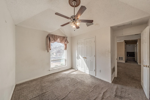 interior space featuring ceiling fan, lofted ceiling, dark carpet, and a textured ceiling