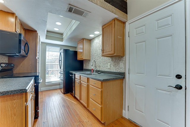 kitchen featuring a raised ceiling, tasteful backsplash, light hardwood / wood-style floors, and black appliances