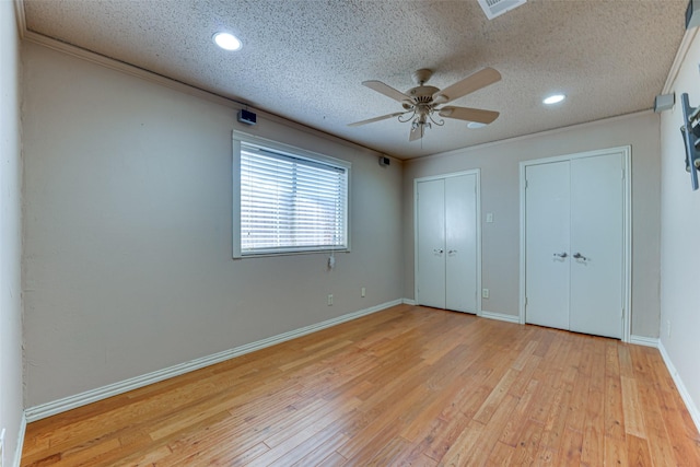 unfurnished bedroom featuring crown molding, two closets, light hardwood / wood-style flooring, and a textured ceiling