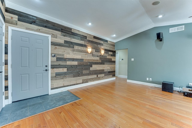 interior space featuring hardwood / wood-style flooring, vaulted ceiling, ornamental molding, and wooden walls