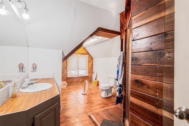 bathroom with hardwood / wood-style floors, vaulted ceiling, vanity, and toilet