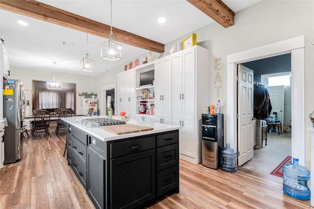 kitchen with appliances with stainless steel finishes, white cabinetry, beam ceiling, a kitchen island, and decorative light fixtures