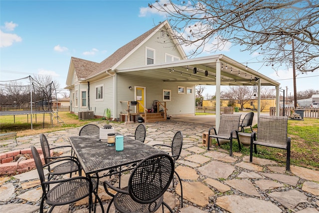 view of patio with a trampoline, central air condition unit, outdoor dining area, fence, and an attached carport