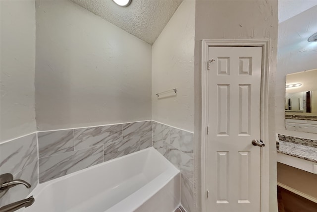 bathroom with vanity, vaulted ceiling, a tub, and a textured ceiling