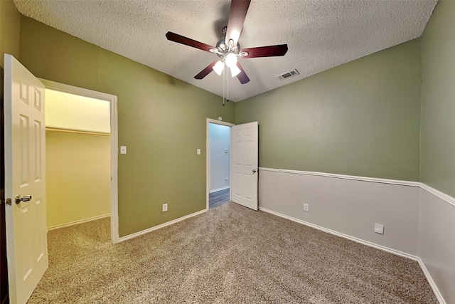 unfurnished bedroom featuring ceiling fan, carpet flooring, a textured ceiling, a walk in closet, and a closet